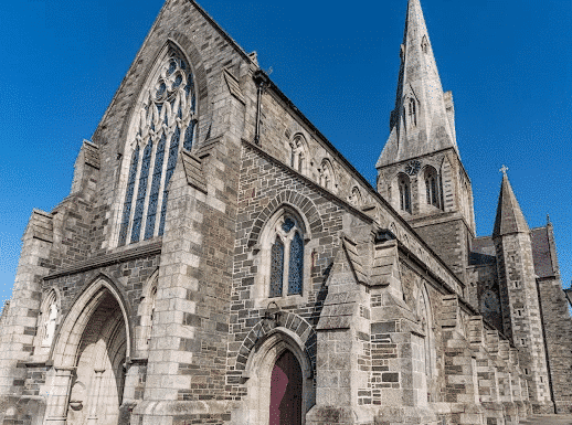 Gothic-style stone church with a tall spire under a blue sky