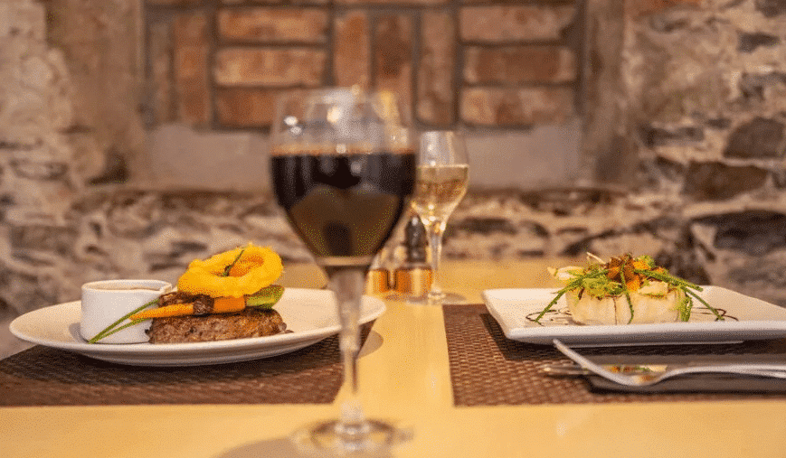Two glasses of red wine on a set table in a dimly lit dining room