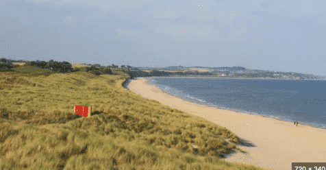 Sandy walking trail through tall grass dunes leading toward a blue sea