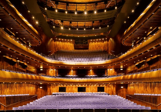 Interior view of a grand theatre auditorium with red velvet seating and gold-leaf tiers