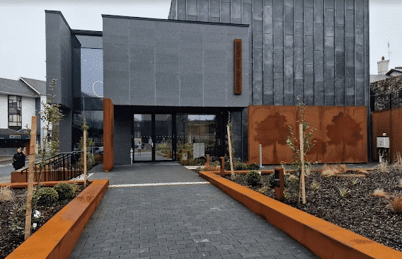 Entrance to a modern building with dark gray angular architecture and a wide stone-paved walkway